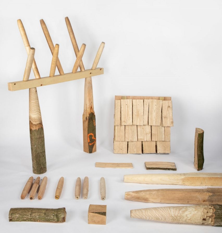 Photo of a number of objects and structures made from small pieces of wood, including a column and beam structure topped by spindles, and another clad with rough wood shingles
