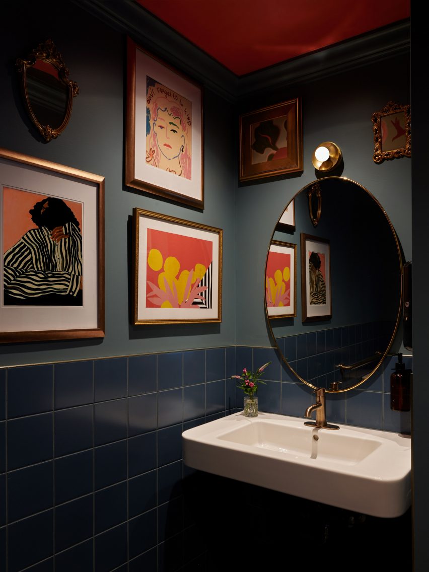 Bathroom with dark blue tiles, paintings on the walls and an oval mirror above a sink