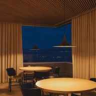 Dining tables overlooking views of the bay by night from a frameless corner window inside a brutalist restaurant in Spain by Zooco Estudio