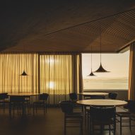 Dining tables overlooking views of the bay from a frameless corner window inside a brutalist restaurant in Spain by Zooco Estudio