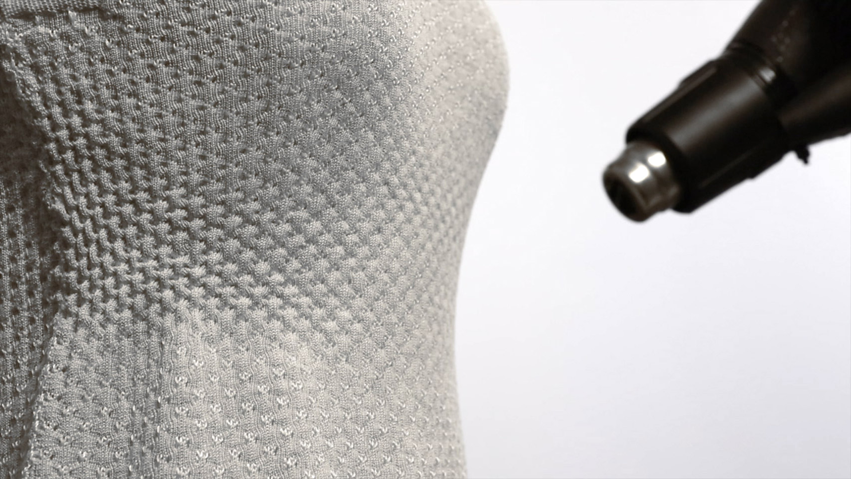 Close-up image of a white knit dress fitted to the bust of a mannequin with a nozzle hovering nearby
