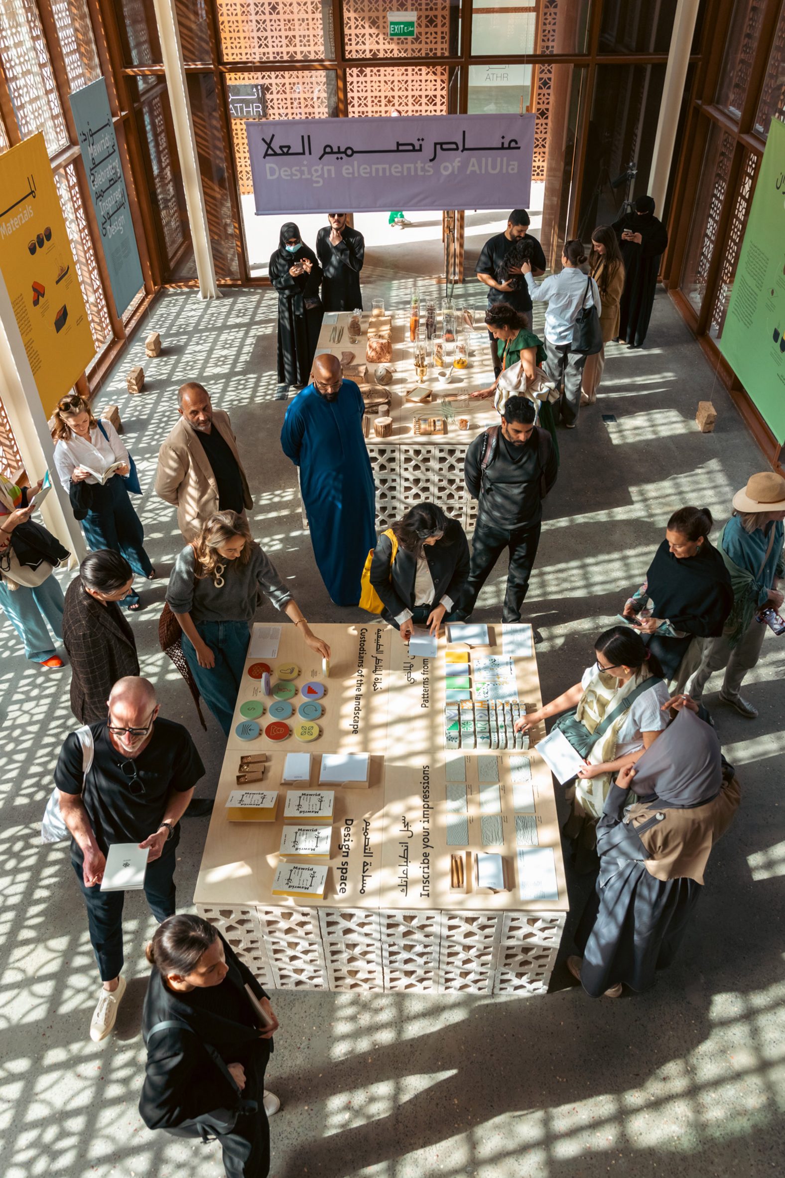 Overhead photo of people milling around a gallery space and looking at displays, amid interesting shadows created by patterned screens