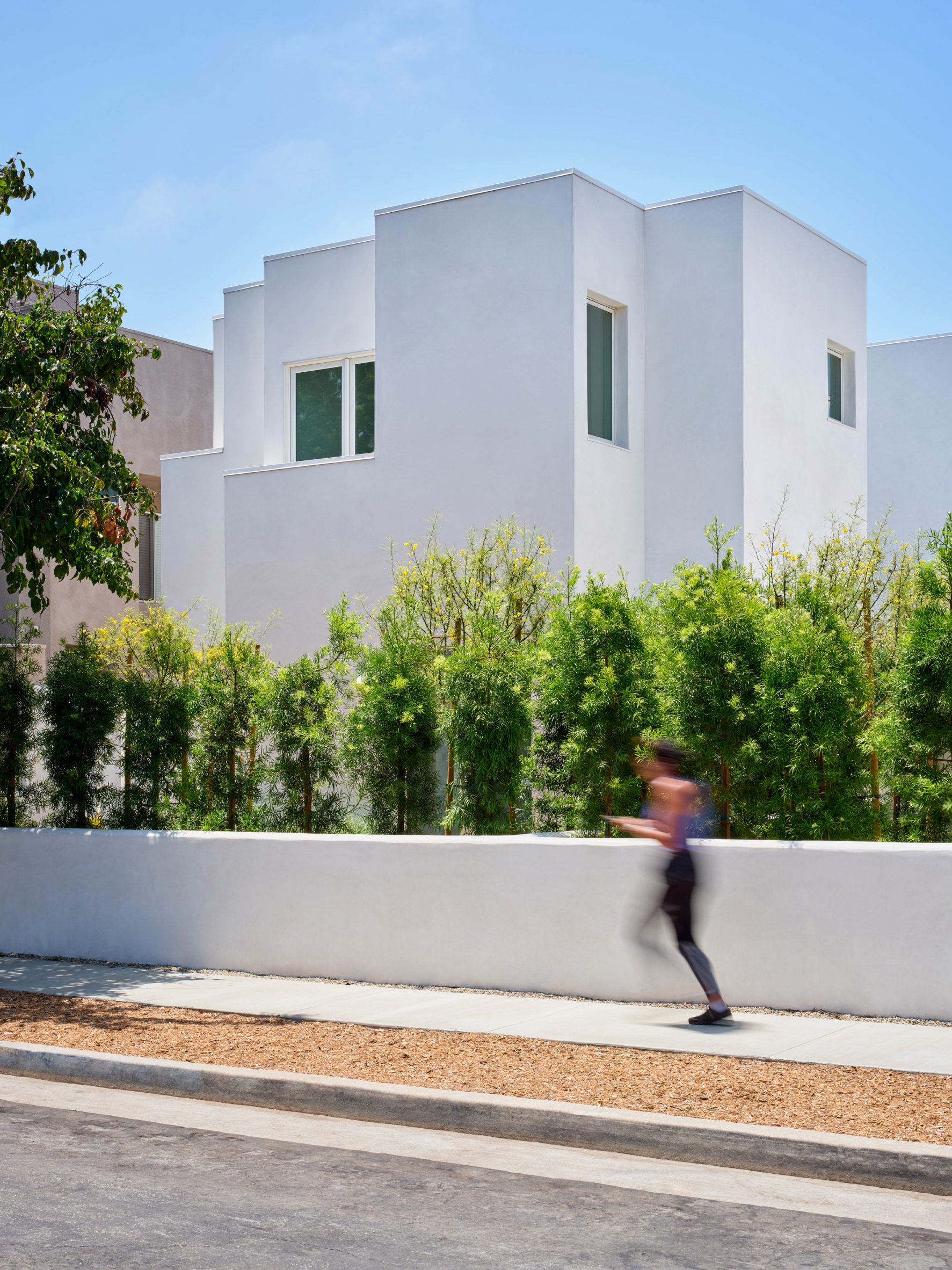 Woman running in front of white stucco house rising out of hedges