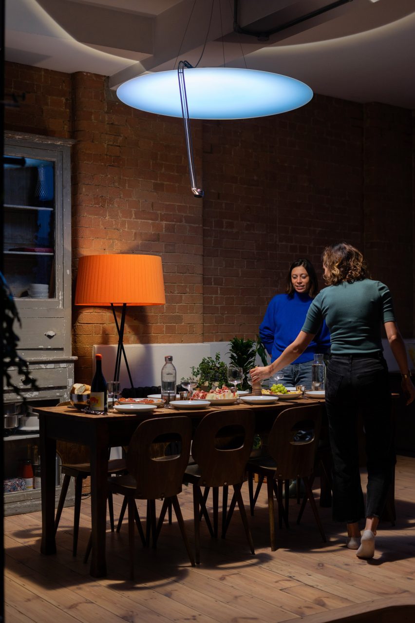 Photo of people milling around a set dining table lit by a large and bright overhead disc