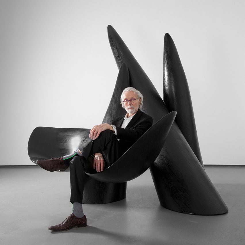 Photo of Wendell Castle in his later years sitting on one of his large, black, biomorphic sculptures