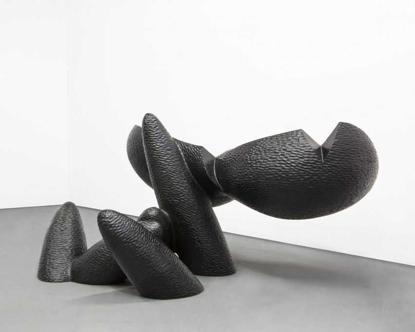 Photo of a large, black sculpture made of bulbous and finger-like organic forms emerging from the ground
