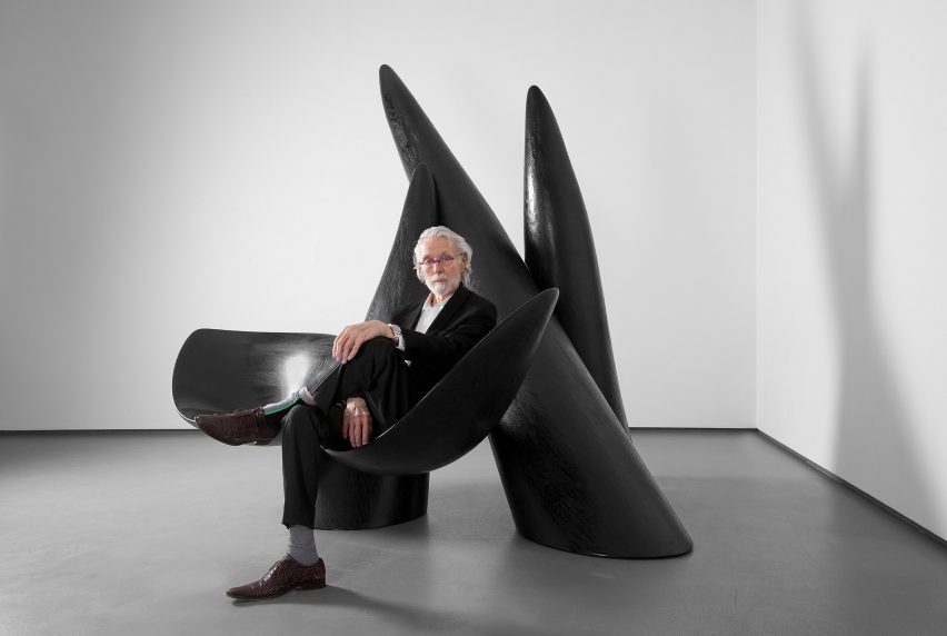 Photo of Wendell Castle in his later years sitting on one of his large, black, biomorphic sculptures