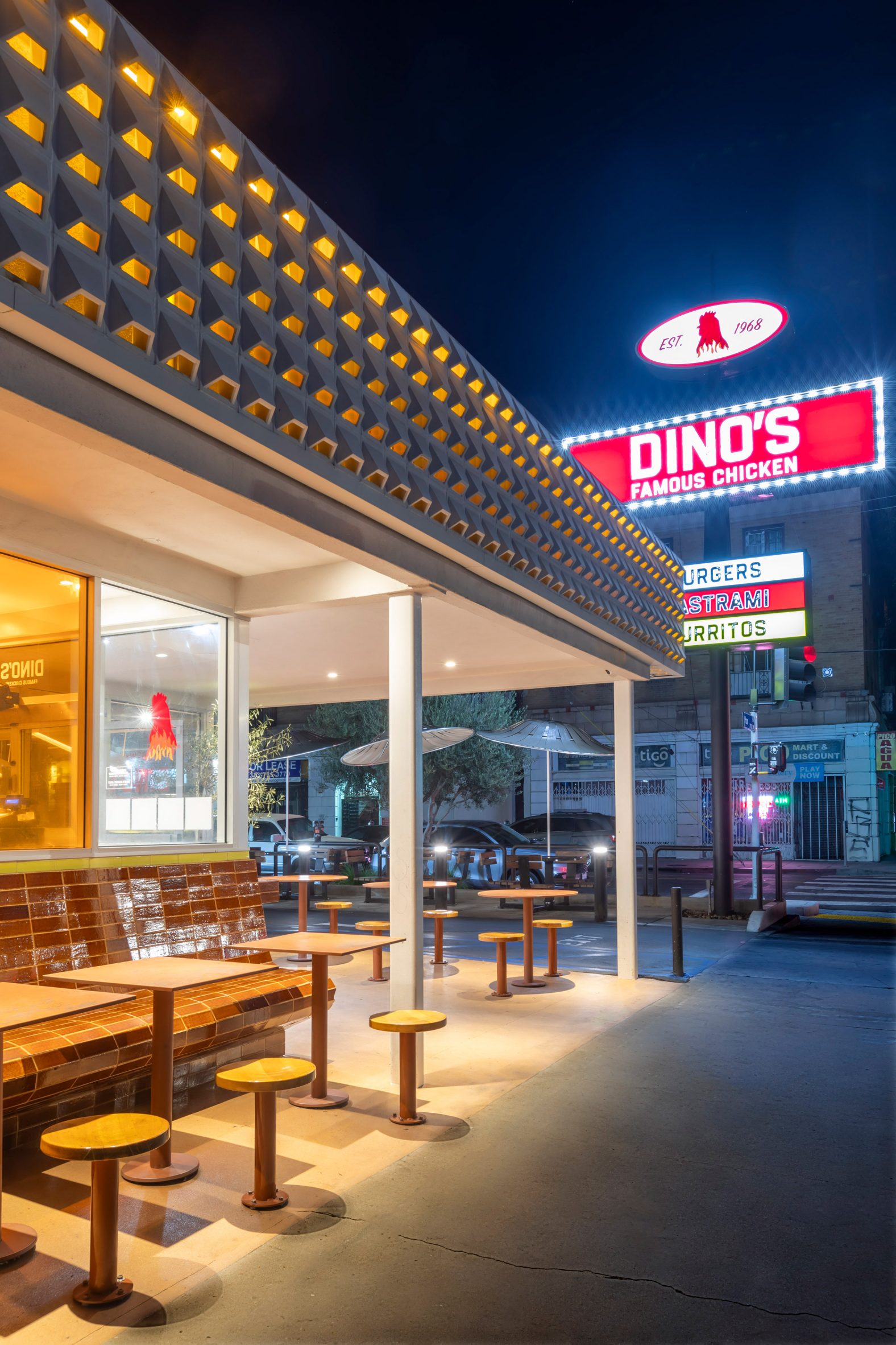 Exterior of Dino's Famous Chicken shop at night with large sign in the background