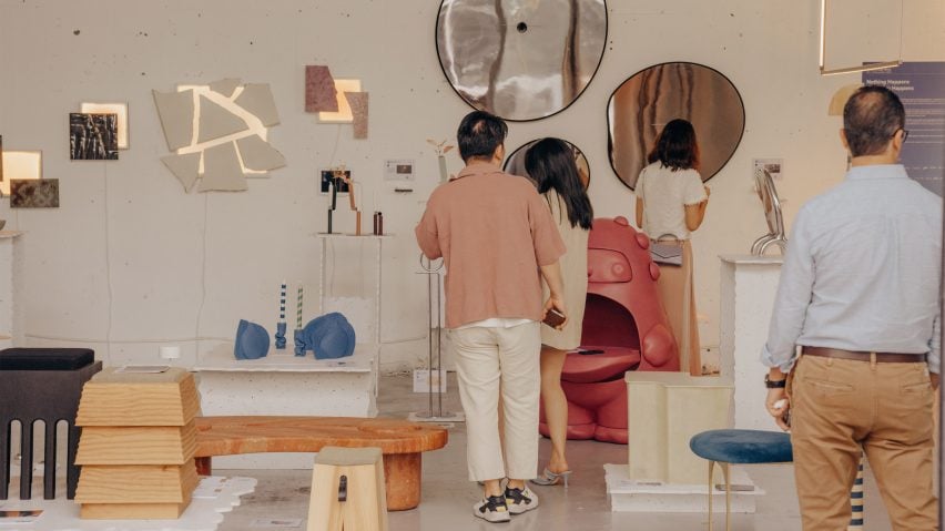 A photograph of an exhibition showcasing interior objects and furniture, with people looking around the space.