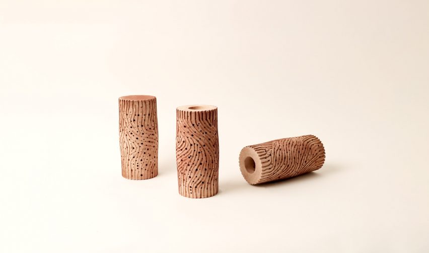 Three cylindrical terracotta vessels on a beige background