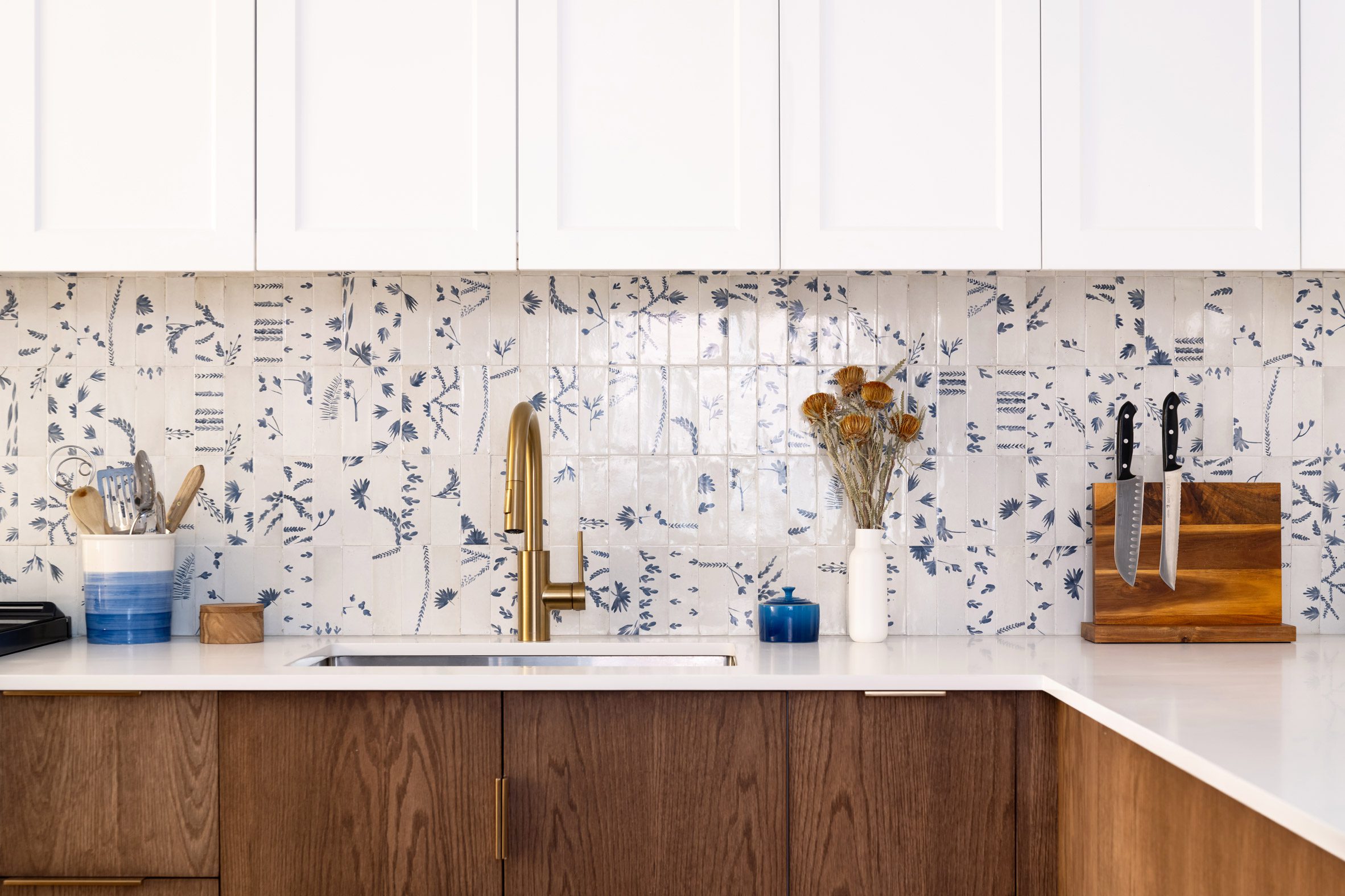 Kitchen with white upper cabinets, blue and white tiled backsplash, and dark oak lower cabinets