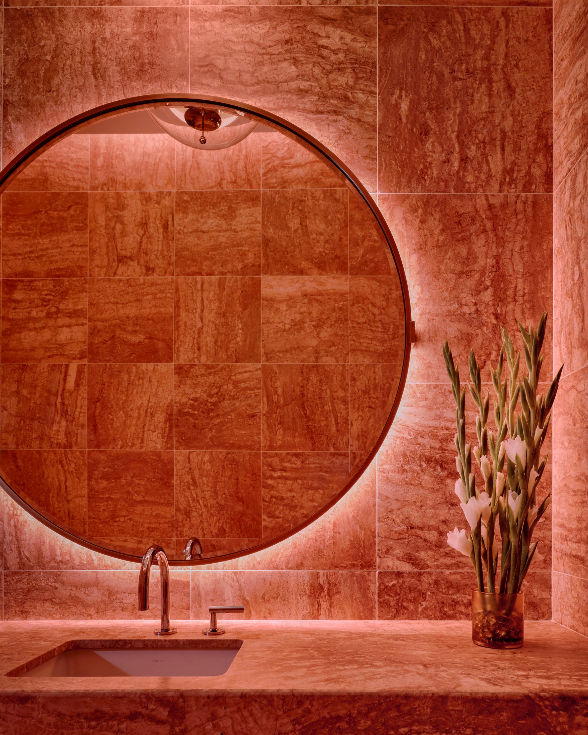 Bathroom with a large circular mirror and walls lined in pink-red stone tiles