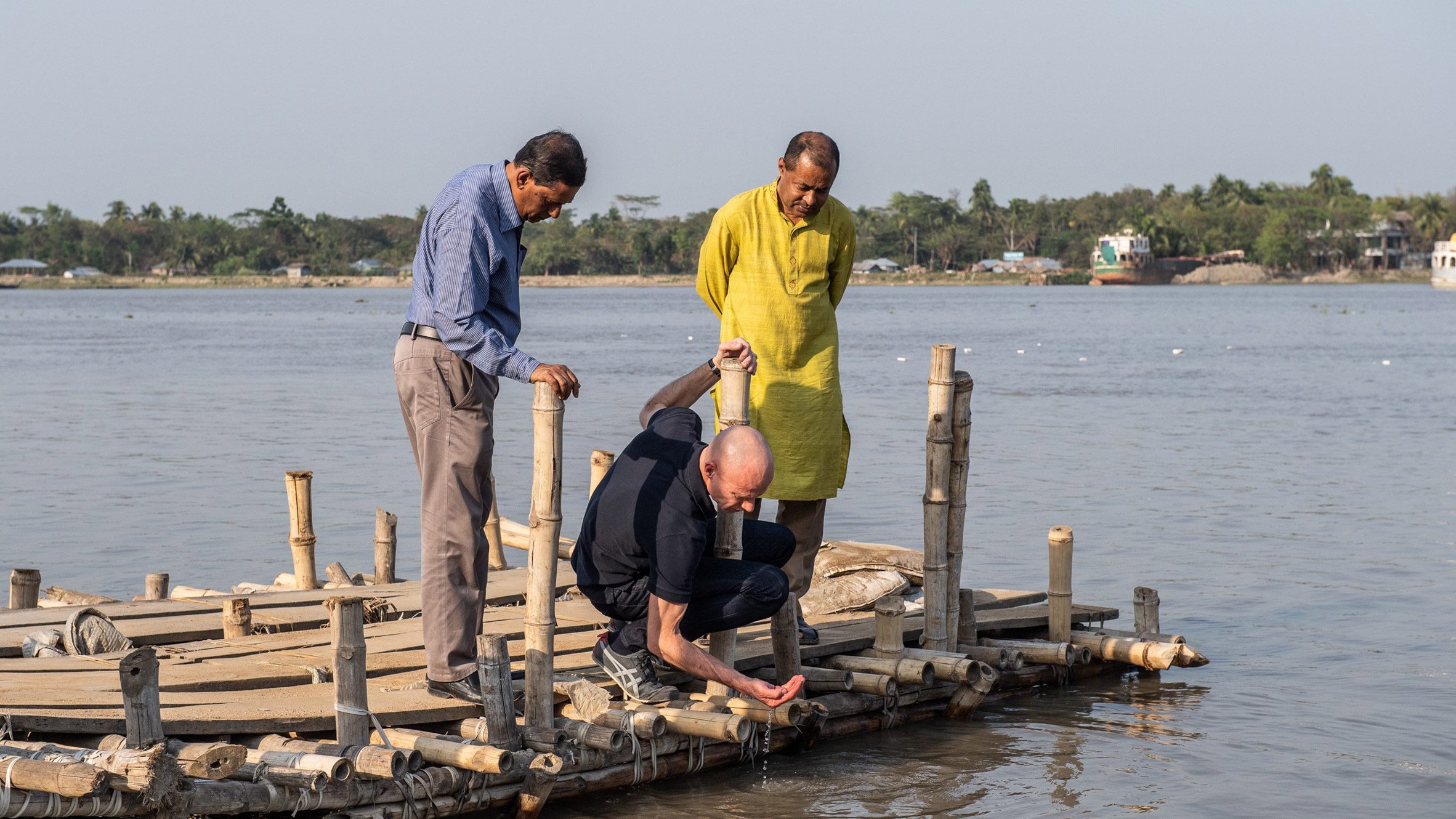 Three men look into water from wooden jetty