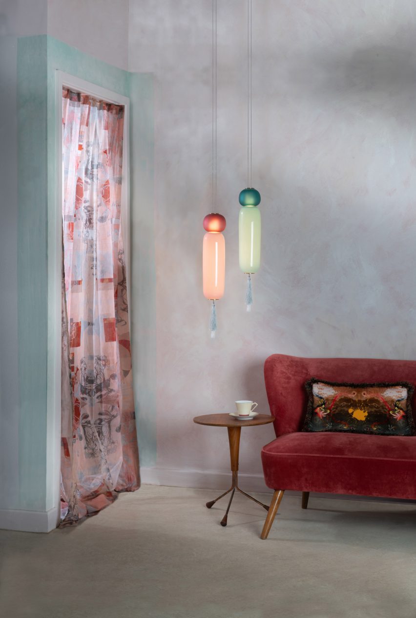 Photo of two Wave II pendant lights, one green and one red, each ending with a tassel, hung in the corner of a living room above a side table