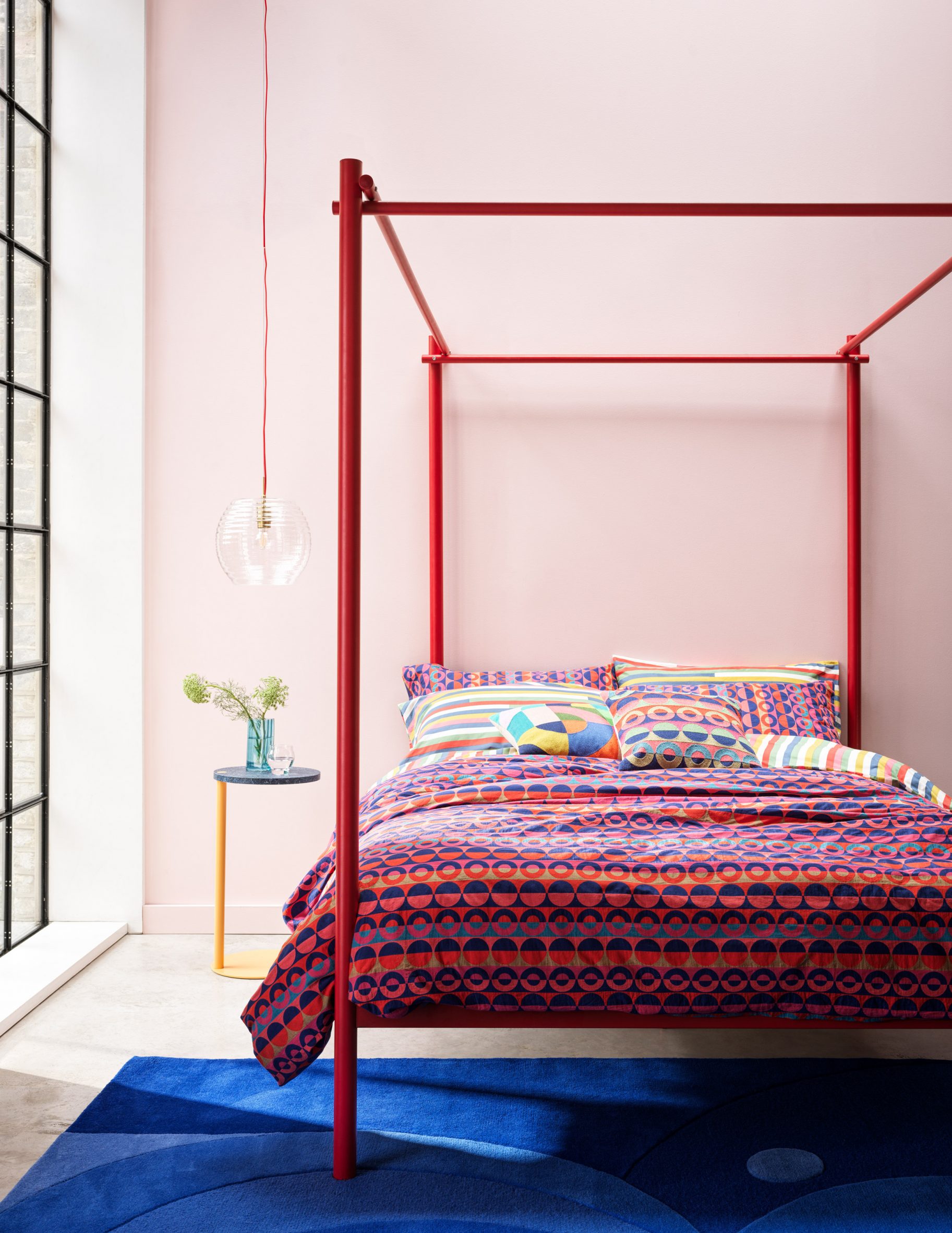Lifestyle photo of bright graphic-print textiles and a red four-poster bed