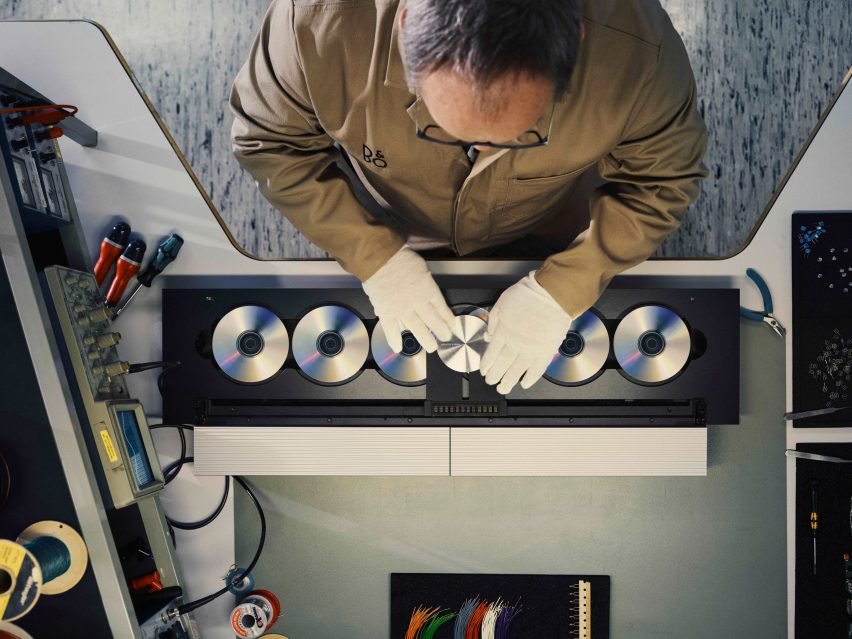Aerial photo of a man in white gloves handling components of a linear six-CD player in a factory