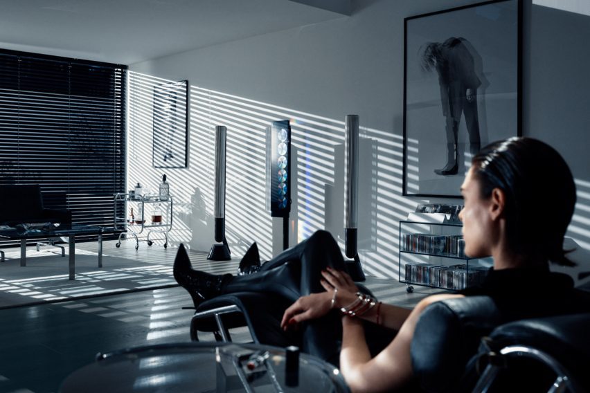 Lifestyle photo of a woman dressed in black with slicked-back hair sitting in a cool, minimalist living room with a Beosystem 9000c CD player unit in the middle