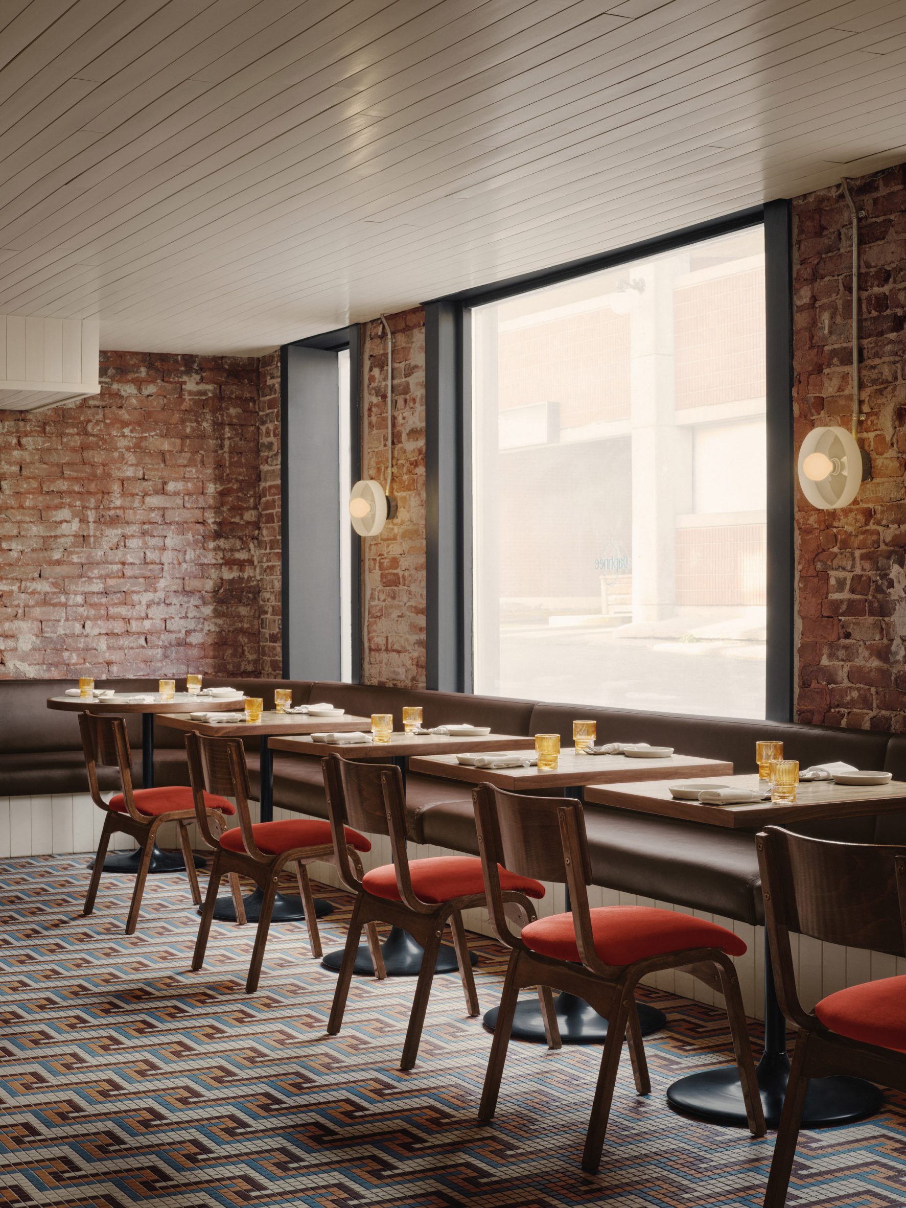 Restaurant interior with glossy cream ceiling, exposed brick walls and brown banquettes