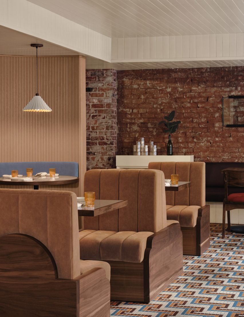 A restaurant interior features exposed brickwork, natural walnut and cognac-toned upholstery