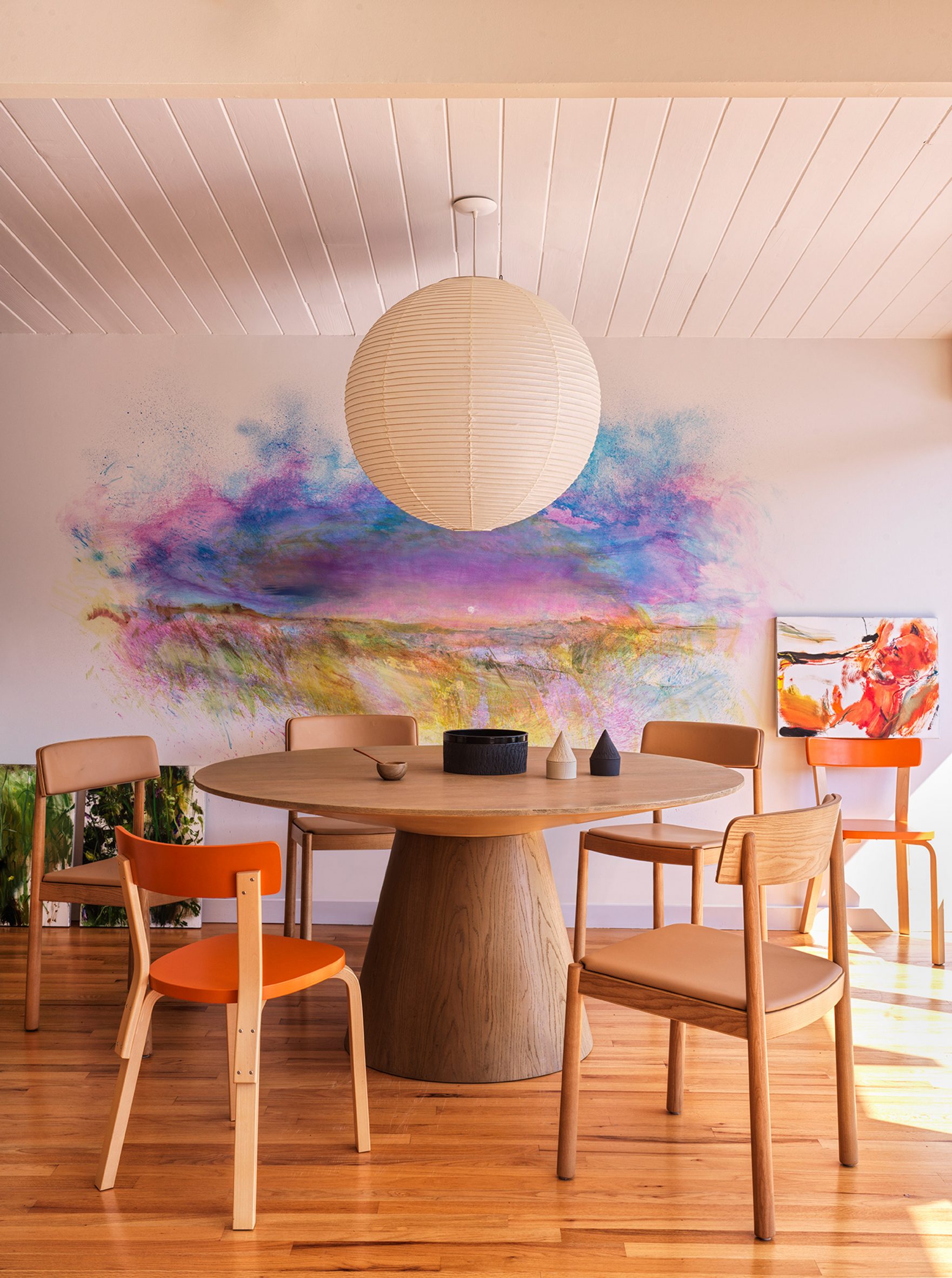 Dining table with spherical pendant lamp and colourful paintings