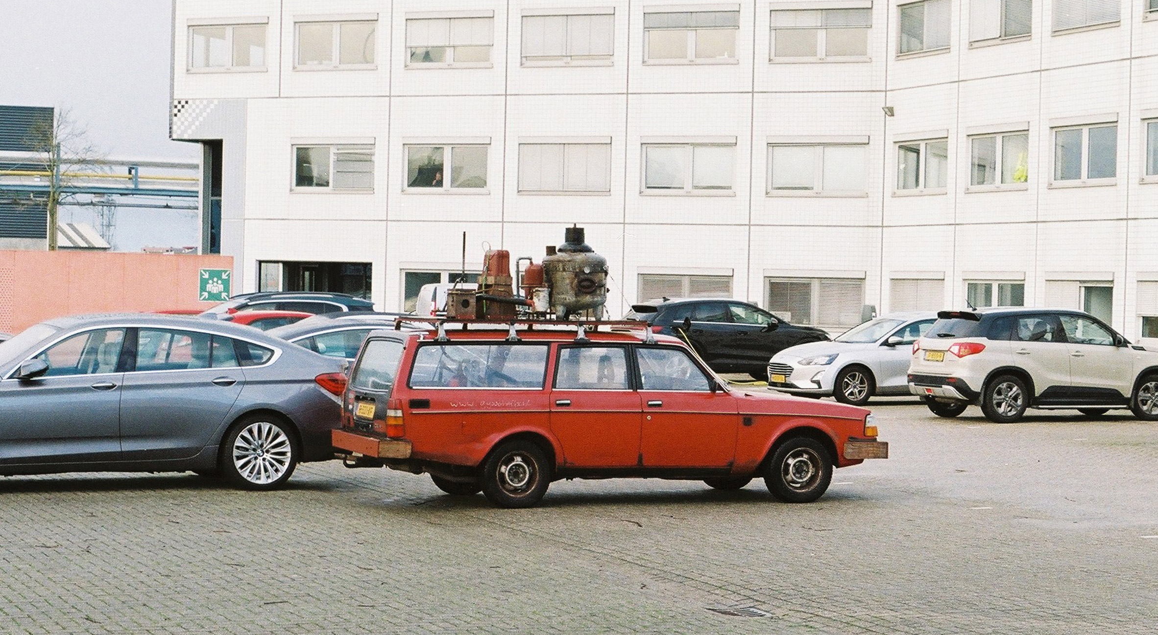 Photo of an old red Volvo with an elaborate contraption on top parked in a car park in front of an apartment building