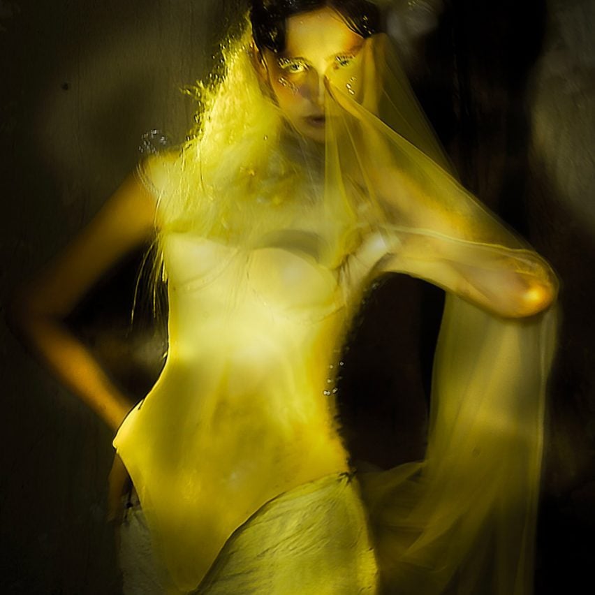 A blurred photograph of a person wearing yellow garments against a dark background.