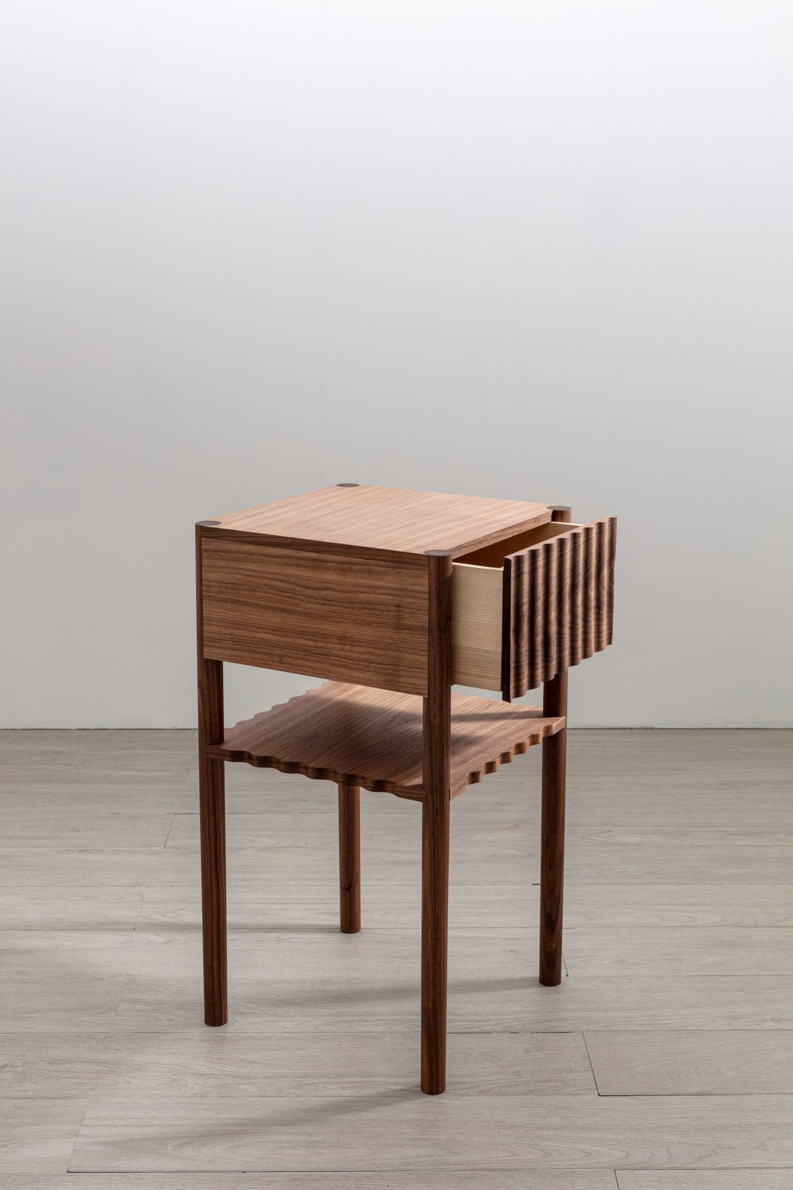 A photograph of a square brown wooden table, placed on a grey floor against a white background.