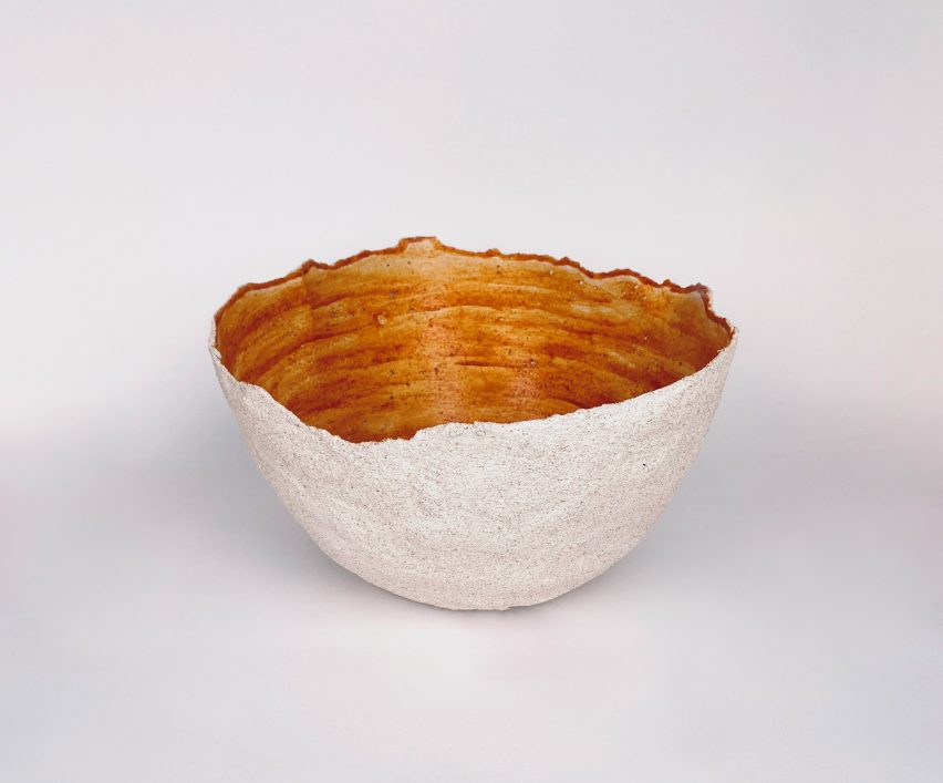 A irregularly shaped bowl, beige on the outside and orange on the inside.