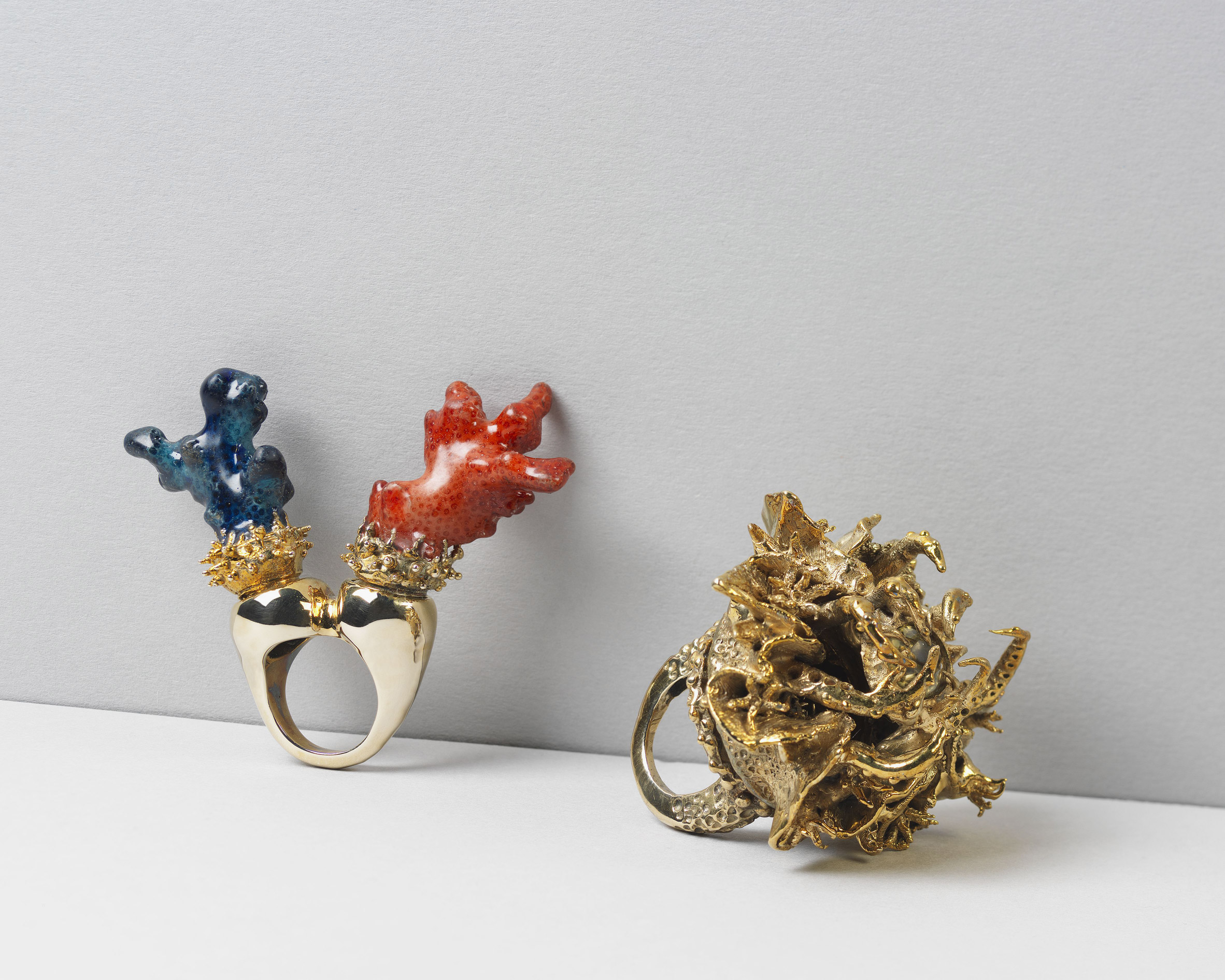 Two gold rings placed on a white surface, one with blue and red embellishing and another with gold embellishing.