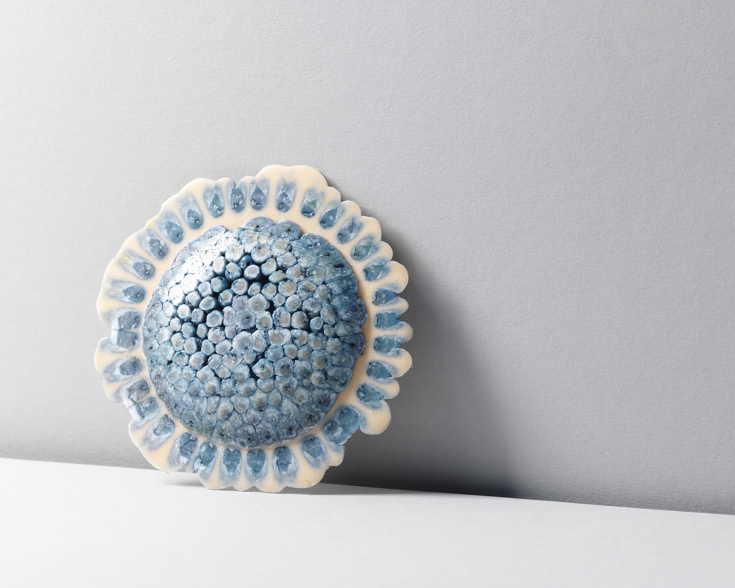 A circular jewellery piece in colours of blue and white against a white background.