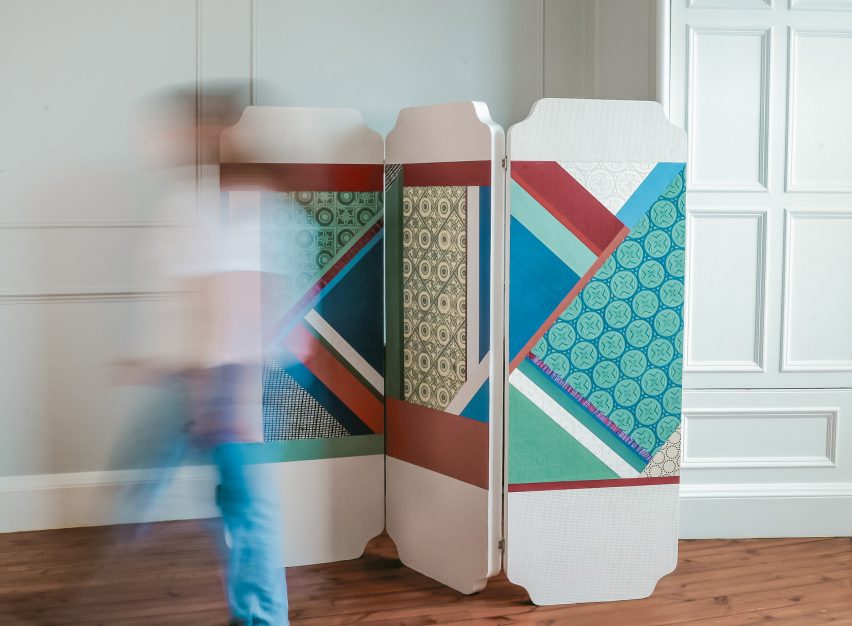 A multicoloured room divider displayed on a wooden floorboard with a person walking in front of it.
