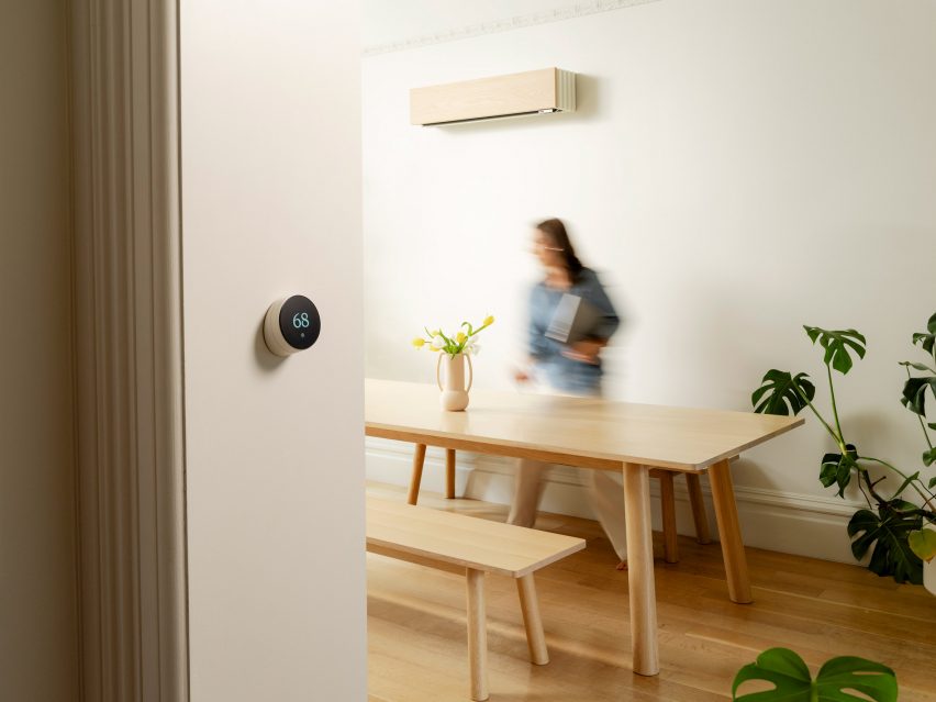 Photo of a woman buzzing about a dining table while an oak-panelled climate unit is wall-mounted above her, and a small circular touchscreen thermostat is visible in the foreground
