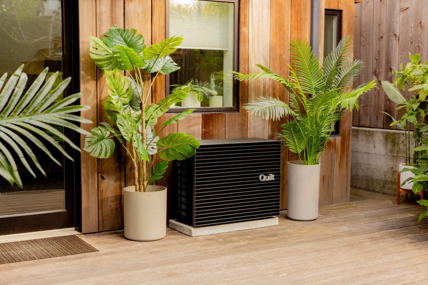 Photo of the Quilt outdoor heat pump unit with a matt black box design, situated between two plants on a front porch