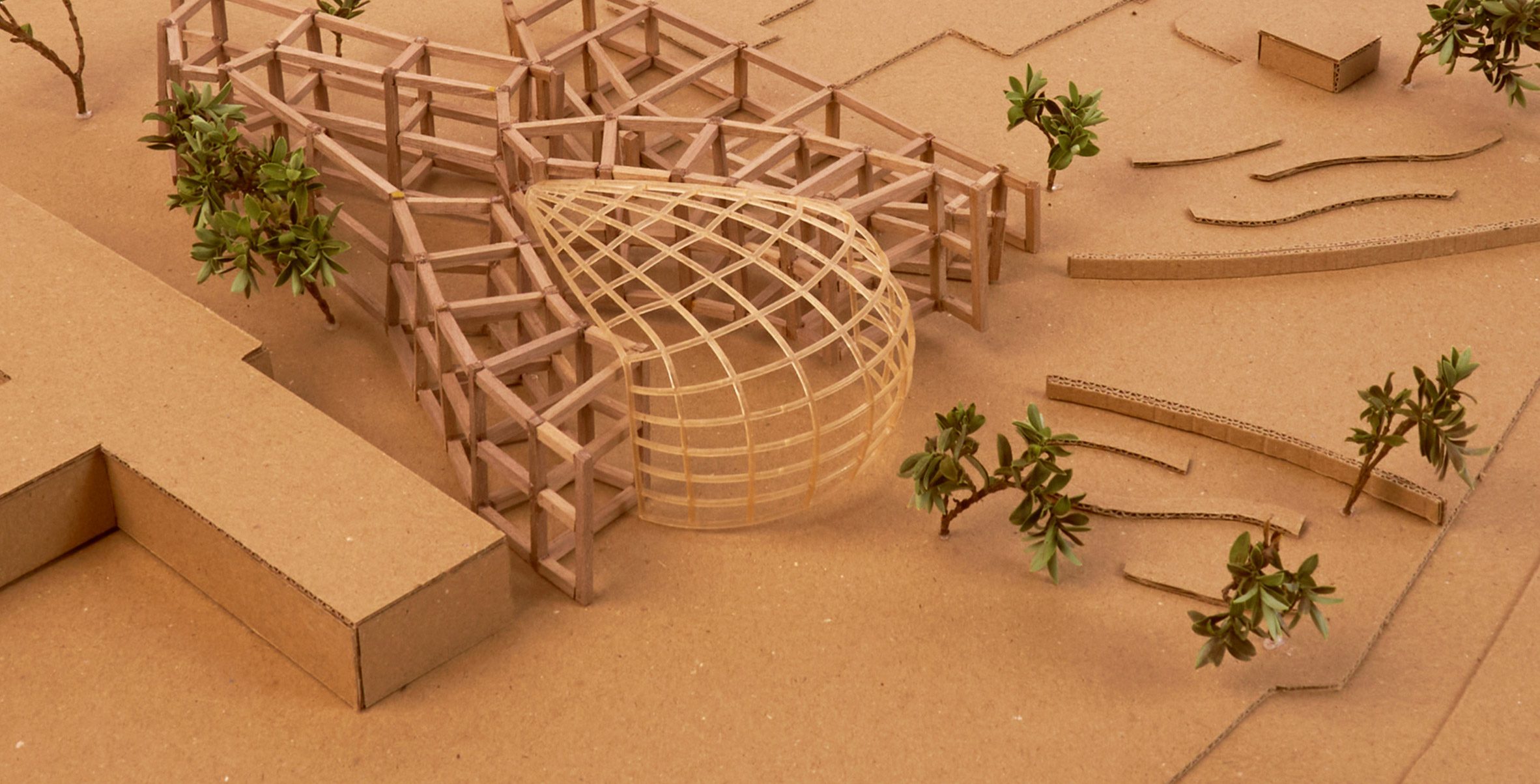 Photograph of an architectural model on a brown surface with brown and green tree models around it.