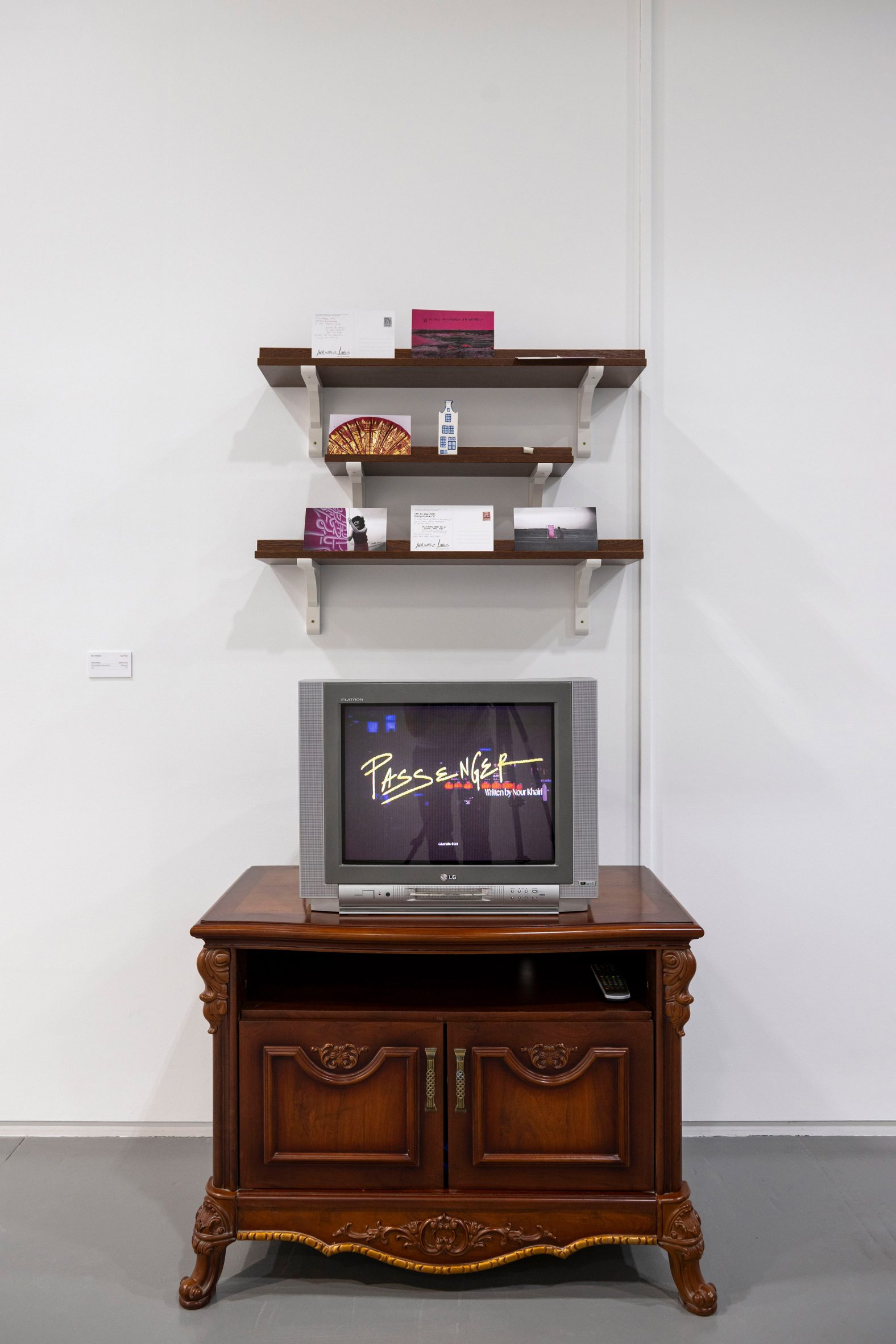 A photograph of a dark brown cabinet against a white wall with a television on top, with three dark brown shelves above.