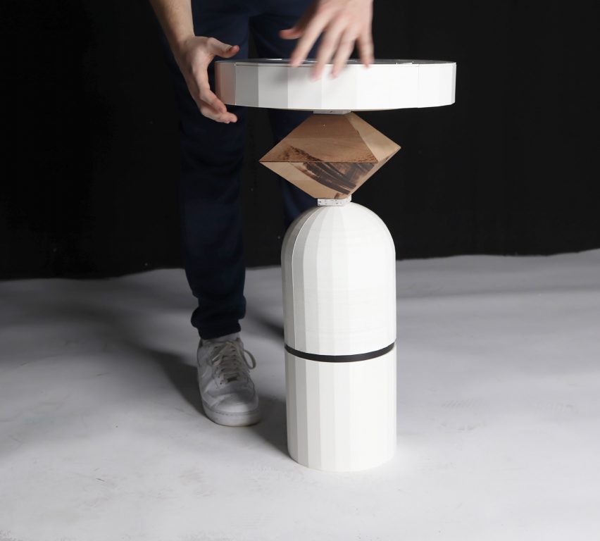 Person handling a white side table with varying circular and diagonal shapes on a white floor.