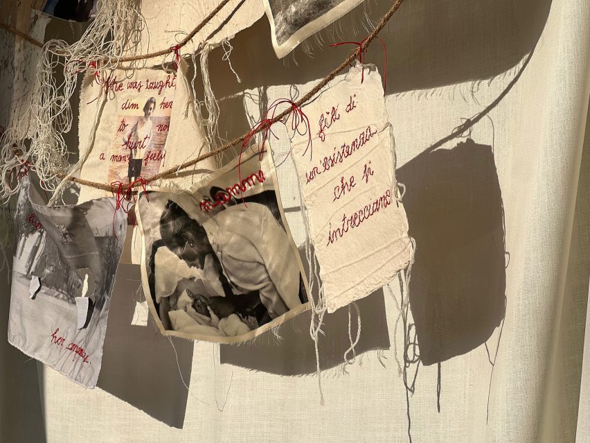 A photograph of various textile sheets hanging from threads. They feature images and red embroidery on them.