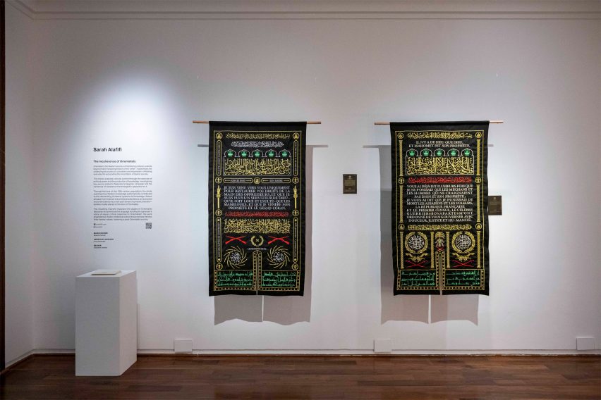 Two tapestries hanging on a white wall, black with yellow, white, green and red embroidery on them.