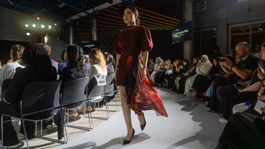 A person walking on a white runway floor in a red dress.