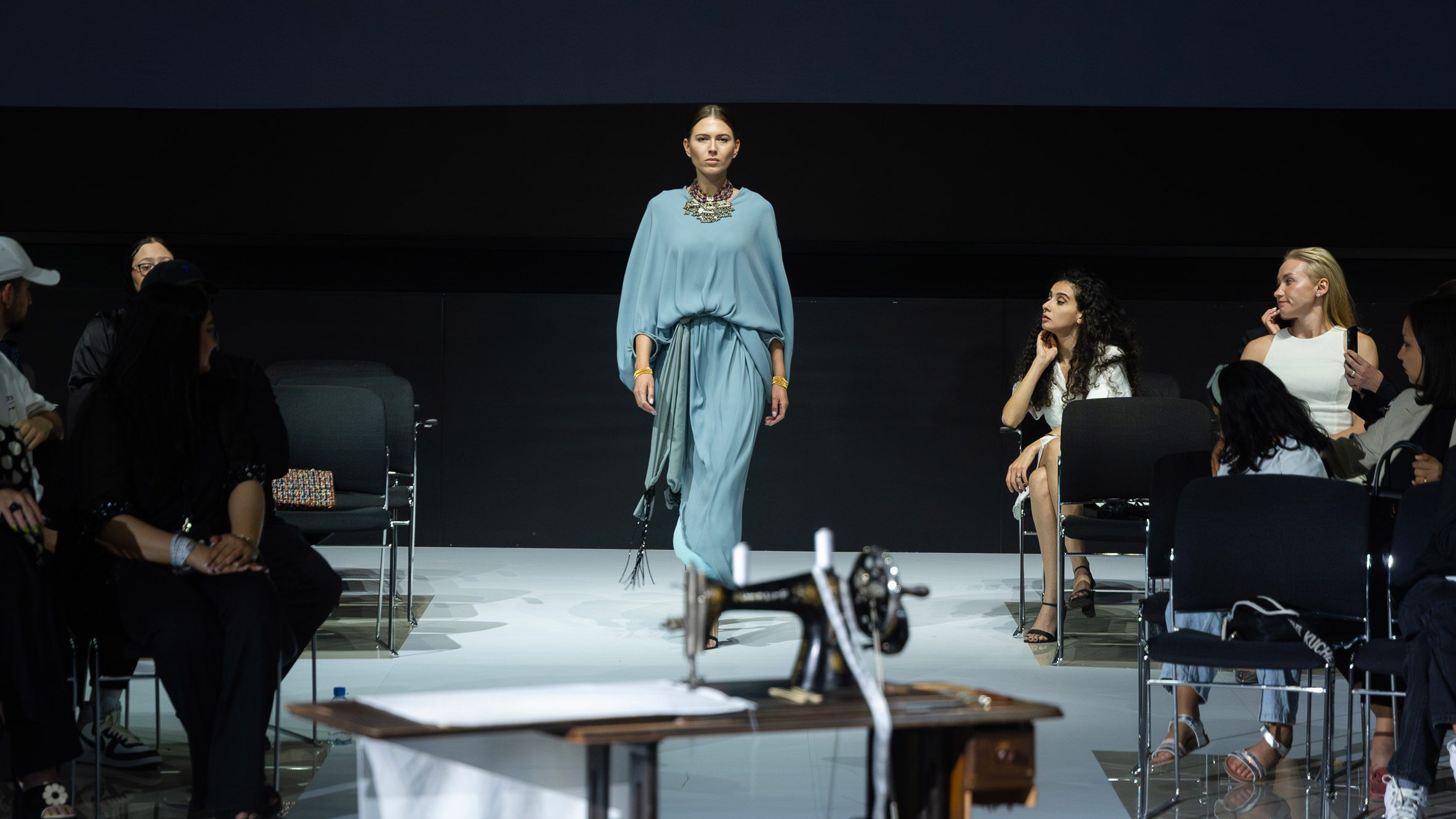 A person walking on a white runway floor with a blue dress on.