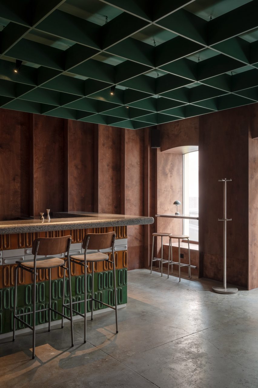 Bar with dark plywood walls and a green coffered ceiling by Mirzoyan Studio