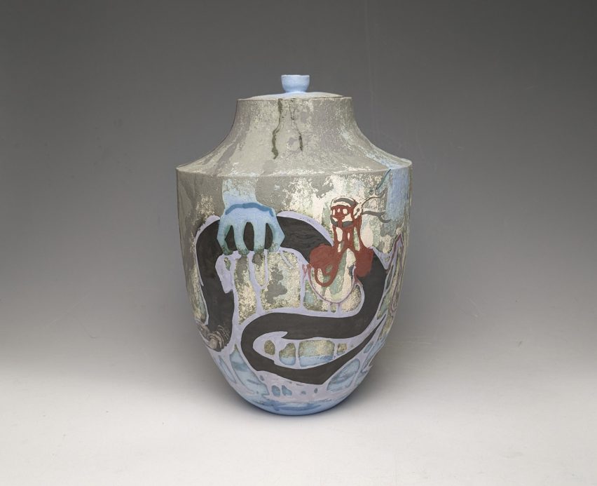 A photograph of a ceramic vase against a grey backdrop, featuring colours of blue, red, lilac and grey.