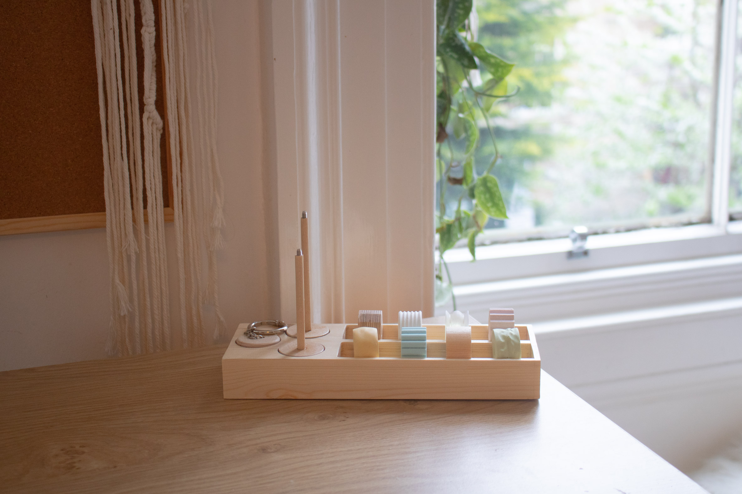 A photograph displaying a product on a table that aids people with ADHD, it features beige coloured wood and different colours of blue, yellow, pink and green. 