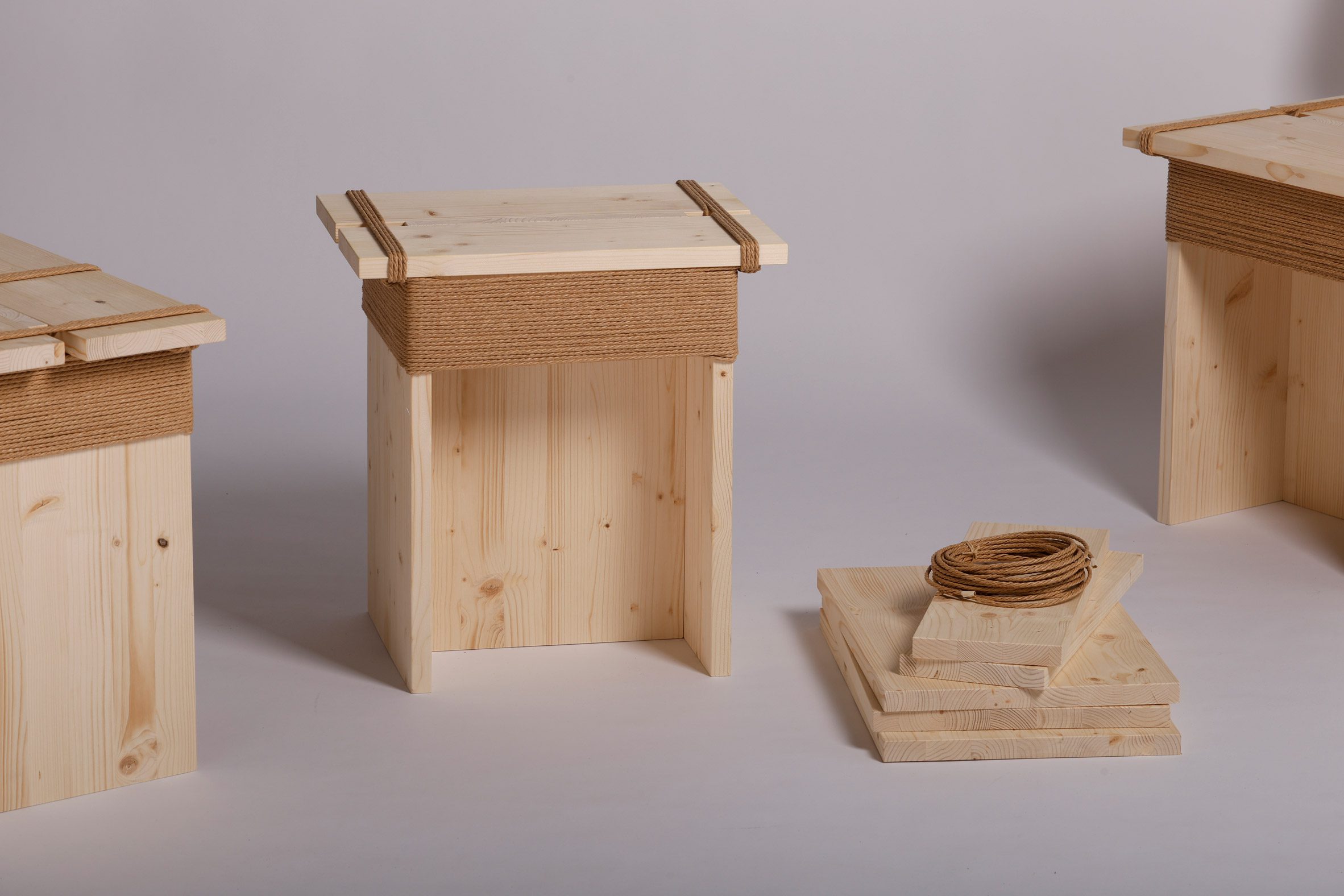 A photograph of three identical beige wooden stools against a white background, with their deconstructed parts laid out in a pile in front of them.