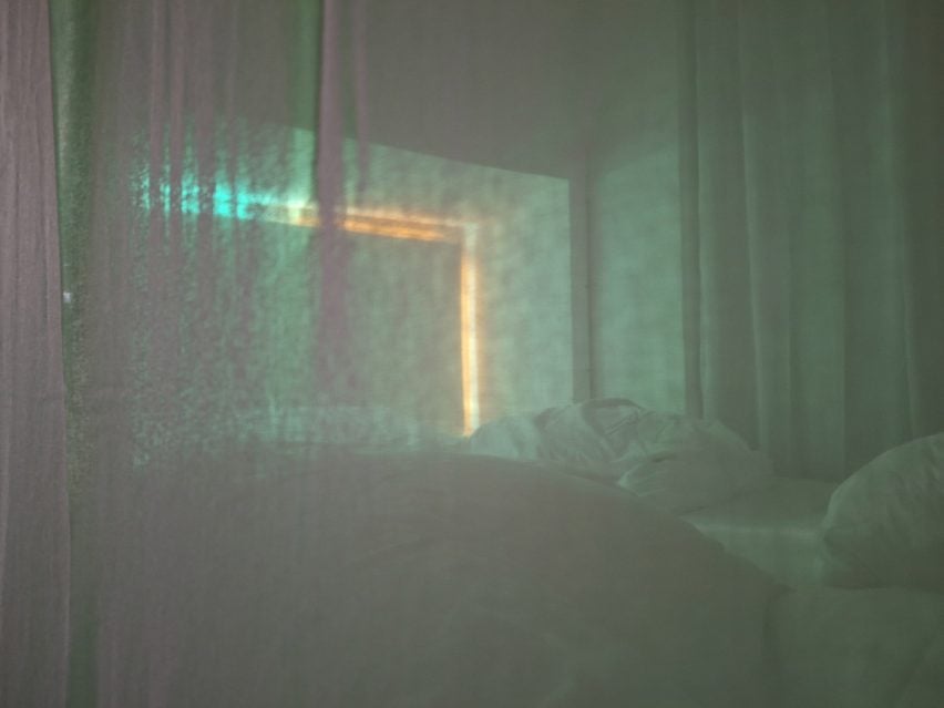 A photograph taken through a fabric sheet of a lounging space in tones of green and orange.