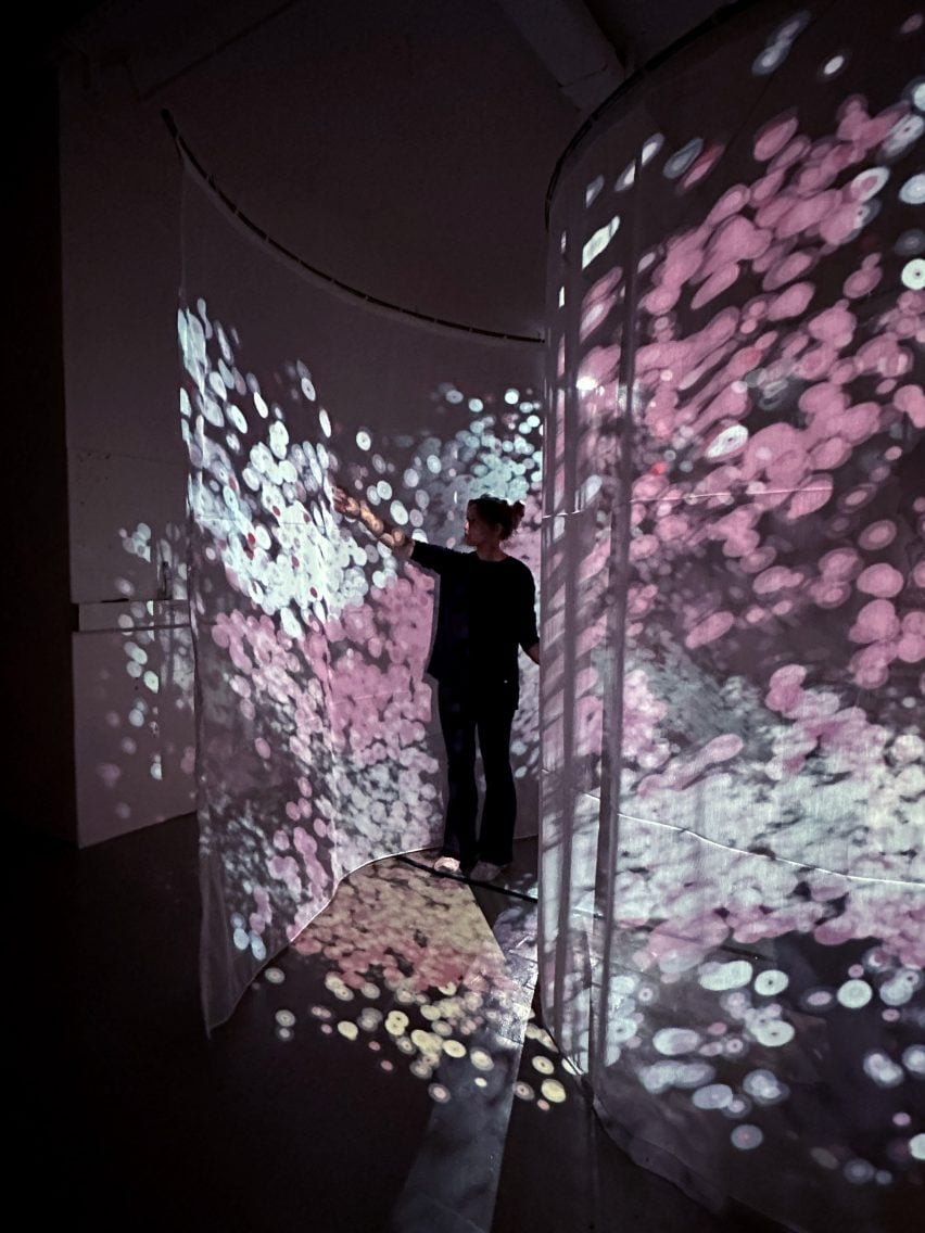 A photograph of a person standing in a space, interacting with an illuminated installation in tones of pink and white.