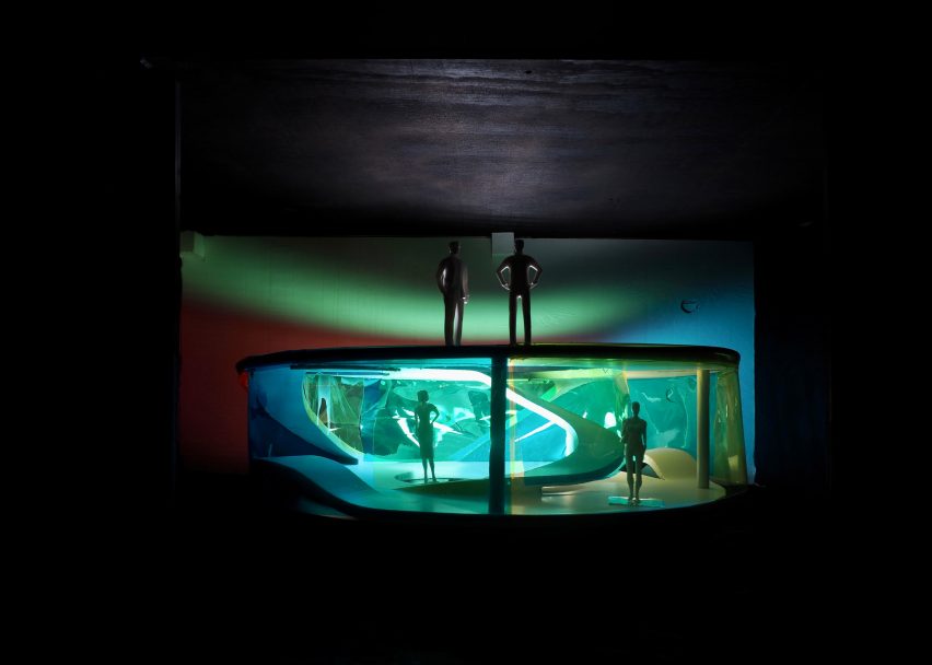 A photograph of an architectural model illuminated in green and blue lighting, with figures in the model.