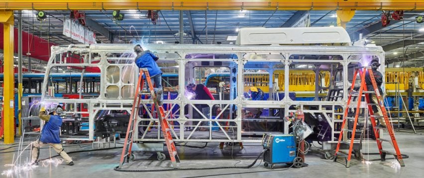 Workers weld parts to the steel frame of an electric public transit bus
