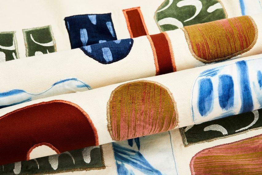 A photograph of rolls of patterned fabric in tones of beige, blue, red and green.