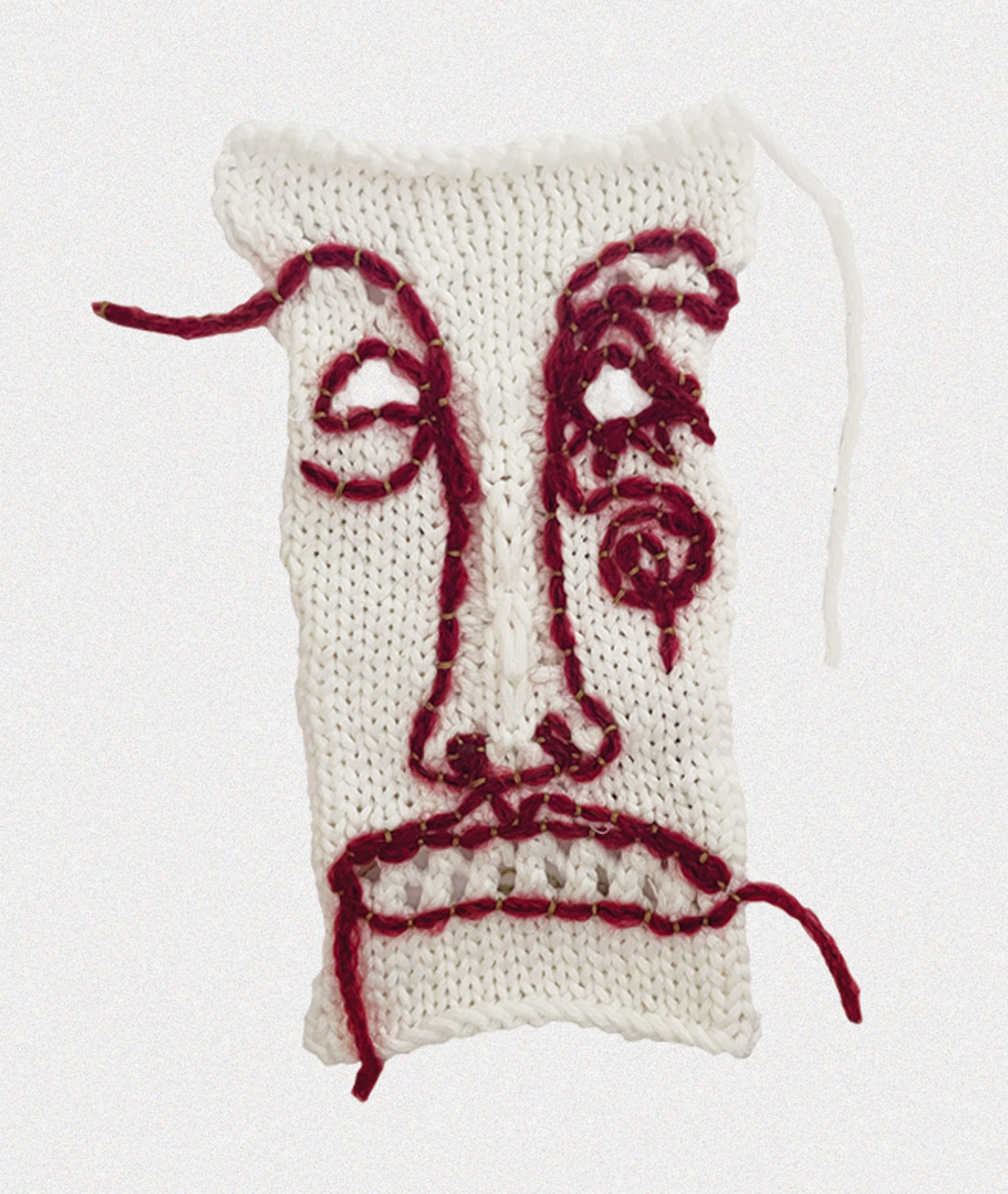 A photograph of a white knitted textile with an abstract face knitted into it in dark red yarn.